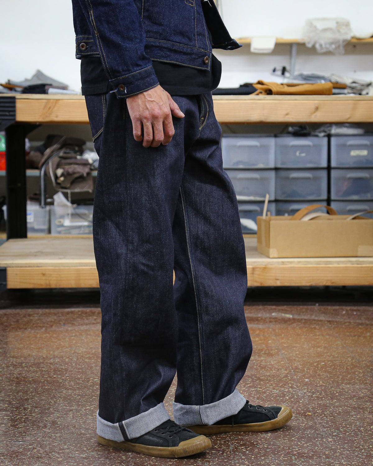 Person wearing dark blue denim pants and shoes in a workshop setting