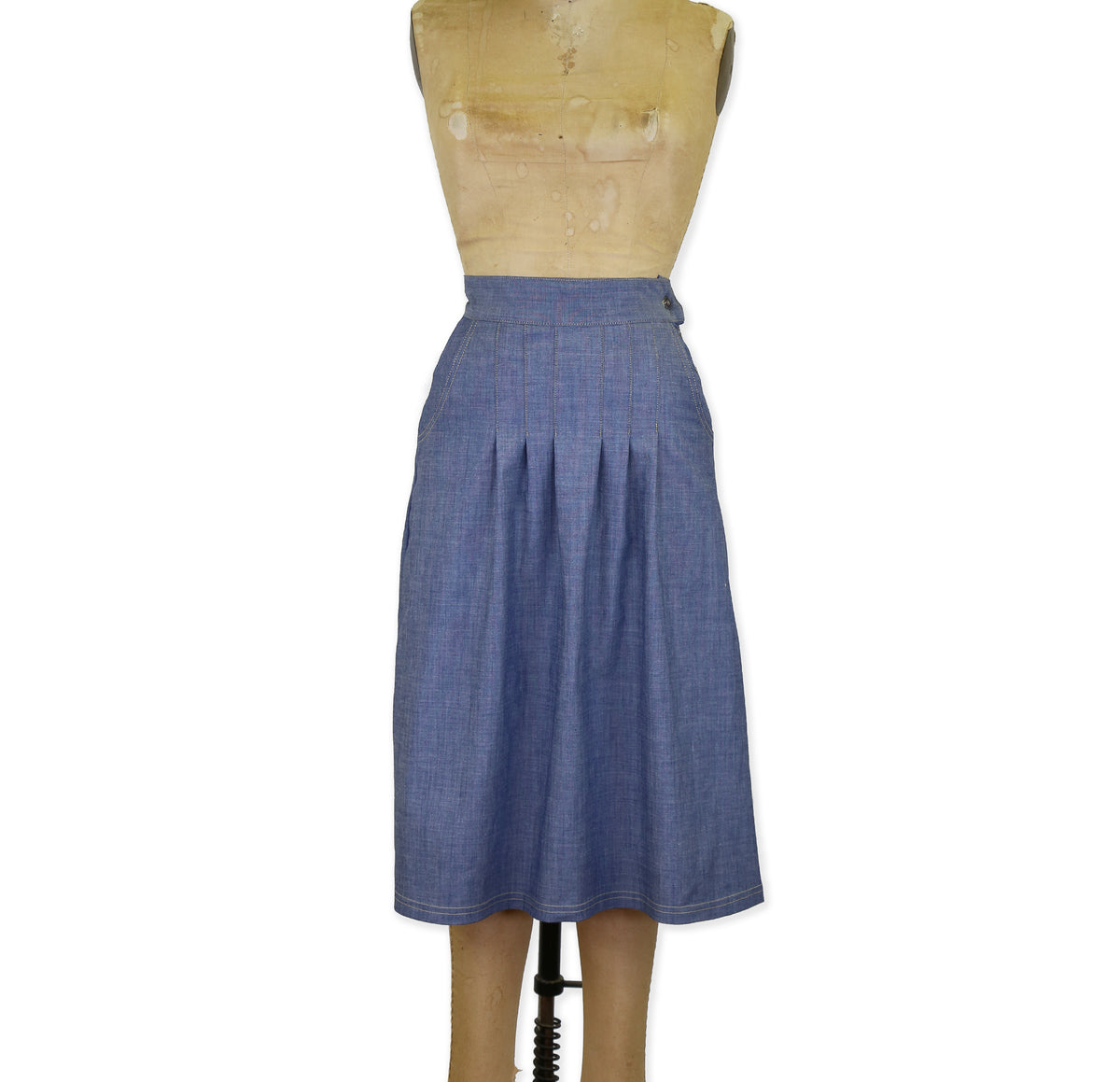 A front pleated chambray indigo skirt with side hand pockets, displayed on a mannequin.