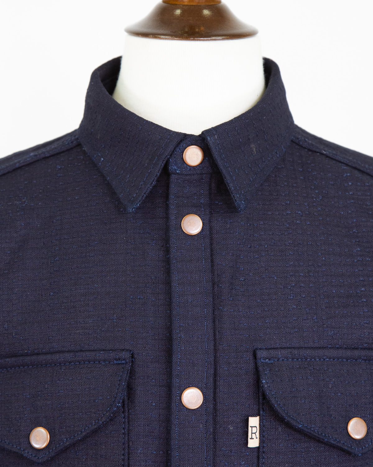 Navy blue shirt with button details on a mannequin against a white background