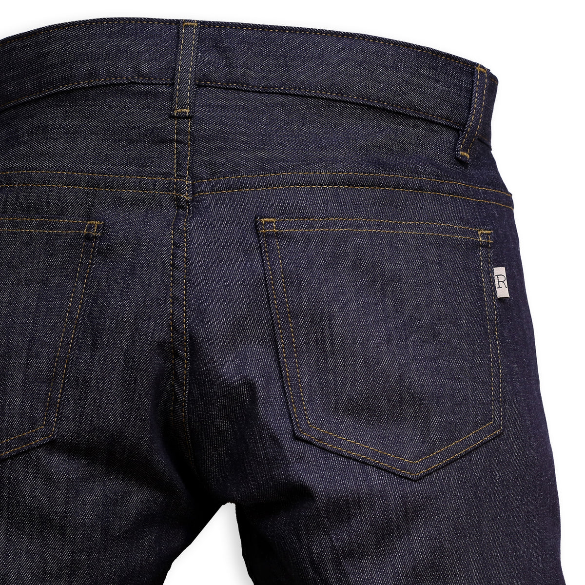 Back Pocket Detail of a pair of slim-fit blue denim jeans with a minimalist design, featuring a small 'R' logo on the back pocket.